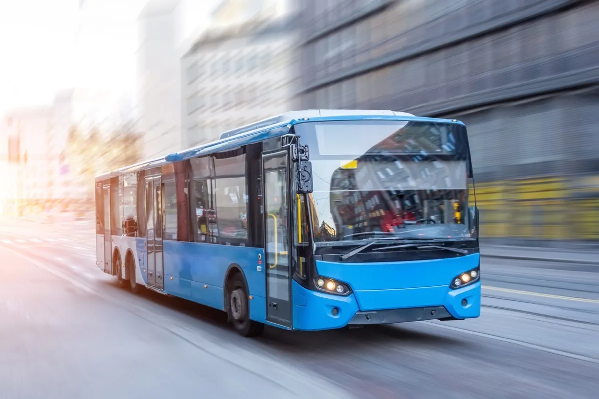 A blue city bus moving along a street, the buildings behind it blurred by its speed.