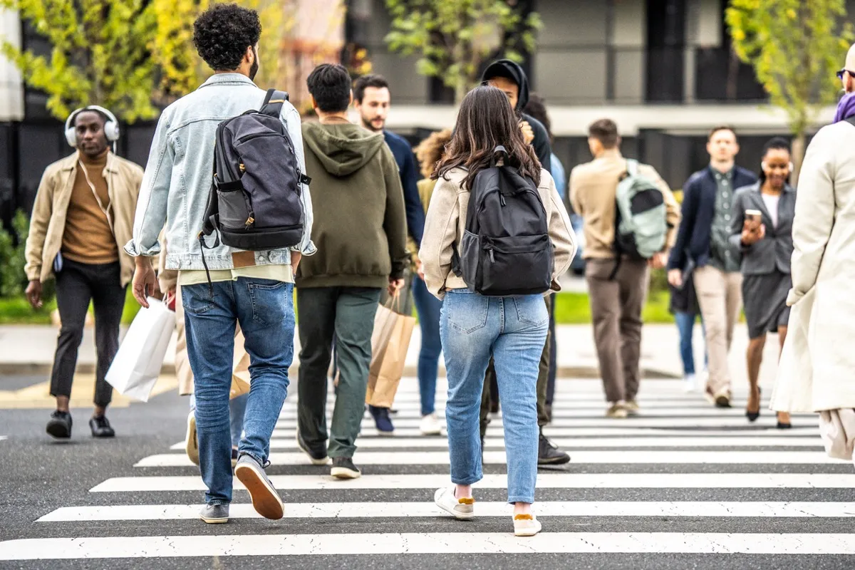 A crowd of pedestrians crossing a city street on a marked crosswalk.