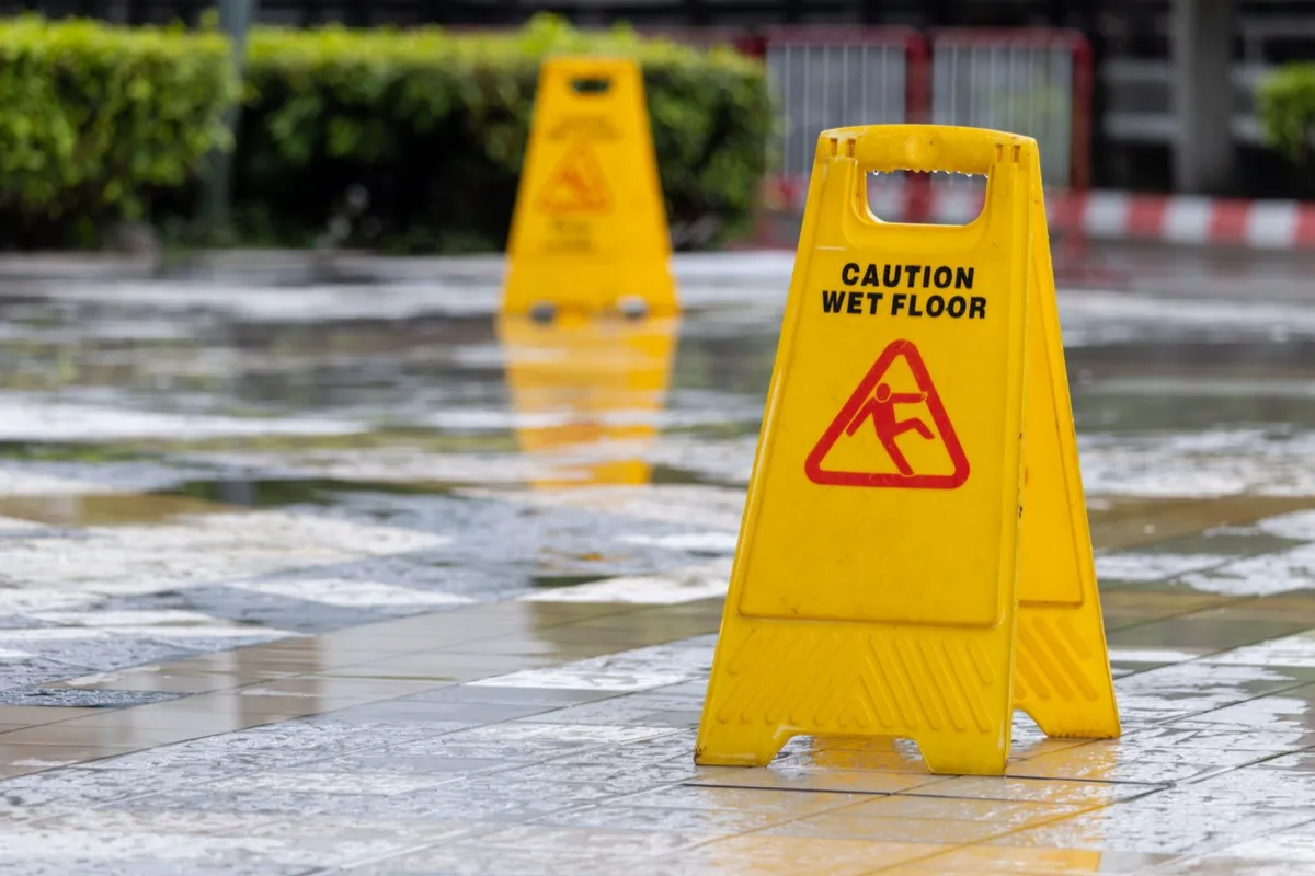 A yellow caution wet floor sign standing on a wet tiled walkway.